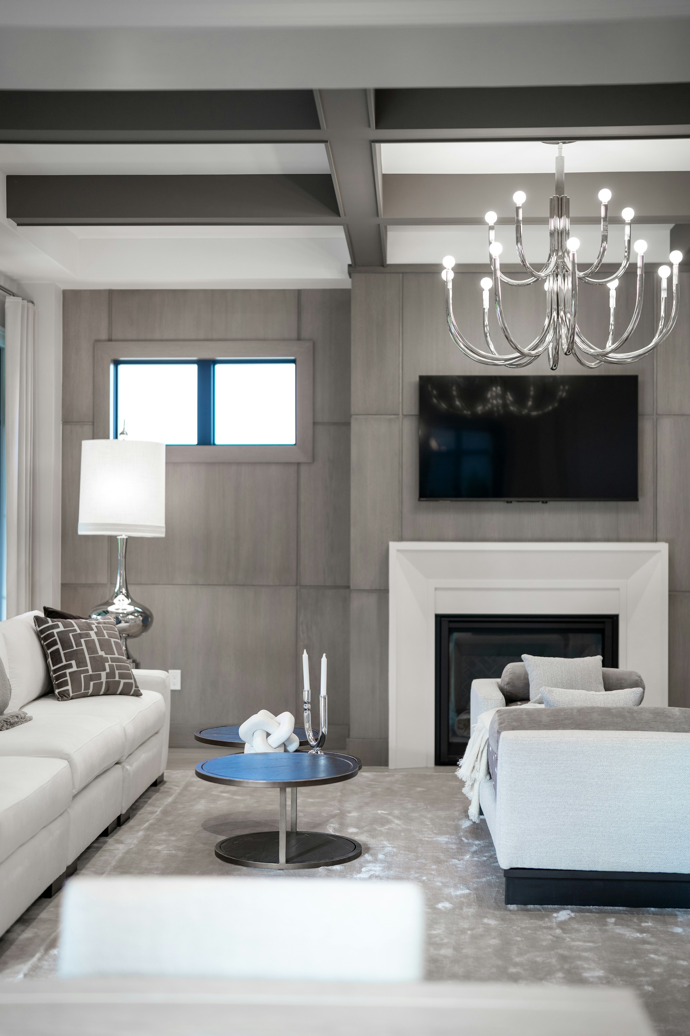 Elegant living room with white sofas, a fireplace, coffered ceiling, and chandelier